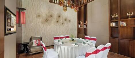 Una mesa redonda con sillas blancas y cintas rojas, ubicada en una habitación con piso de madera y una lámpara decorativa en el techo.