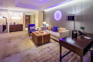 Una habitación de hotel moderna con sofá, una mesa de centro, escritorio y televisor montado en la pared.