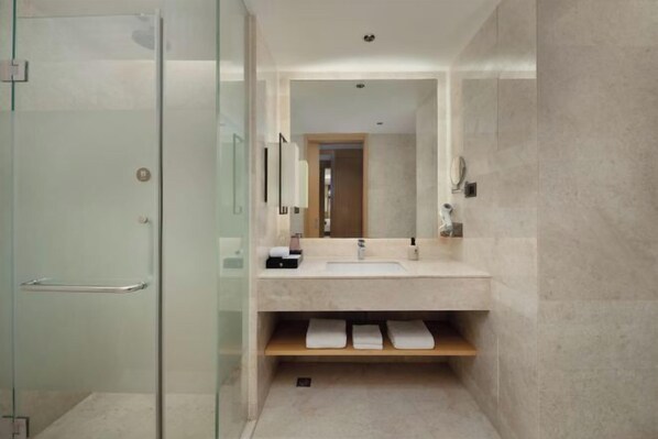 Un baño moderno con cabina de ducha de vidrio, un lavamanos con espejo y un estante de madera con toallas.
