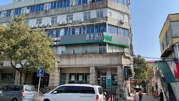 Un bâtiment avec une enseigne verte indiquant un hôtel, une enseigne bleue indiquant un parking, et un arbre devant.