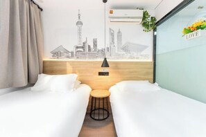 A hotel room with two beds, a small round table, a cityscape mural on the wall, and a 'LOVE' sign on the window.