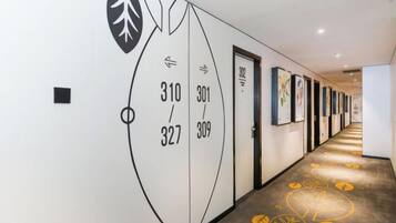 A hallway with numbered doors, artwork on the walls, and a patterned carpet.