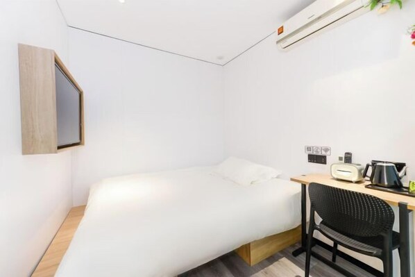 A small, modern room with a bed, a desk, a chair, and a wall-mounted air conditioner.