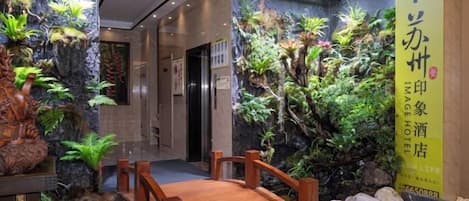 A hotel lobby with a wooden bridge, indoor plants, and a large yellow banner with Chinese characters.