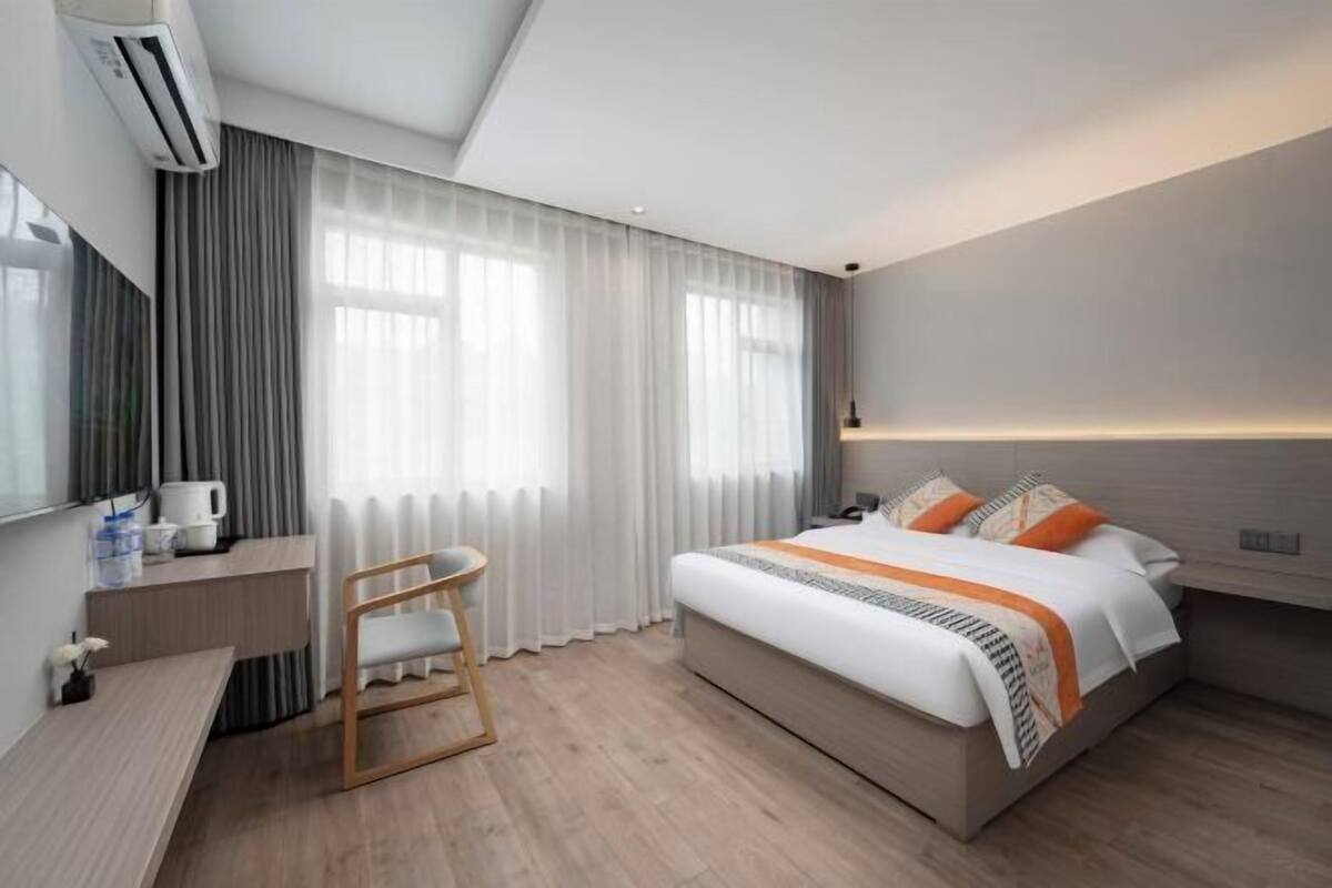A modern hotel room with a bed, a desk, a chair, and a large window with curtains.