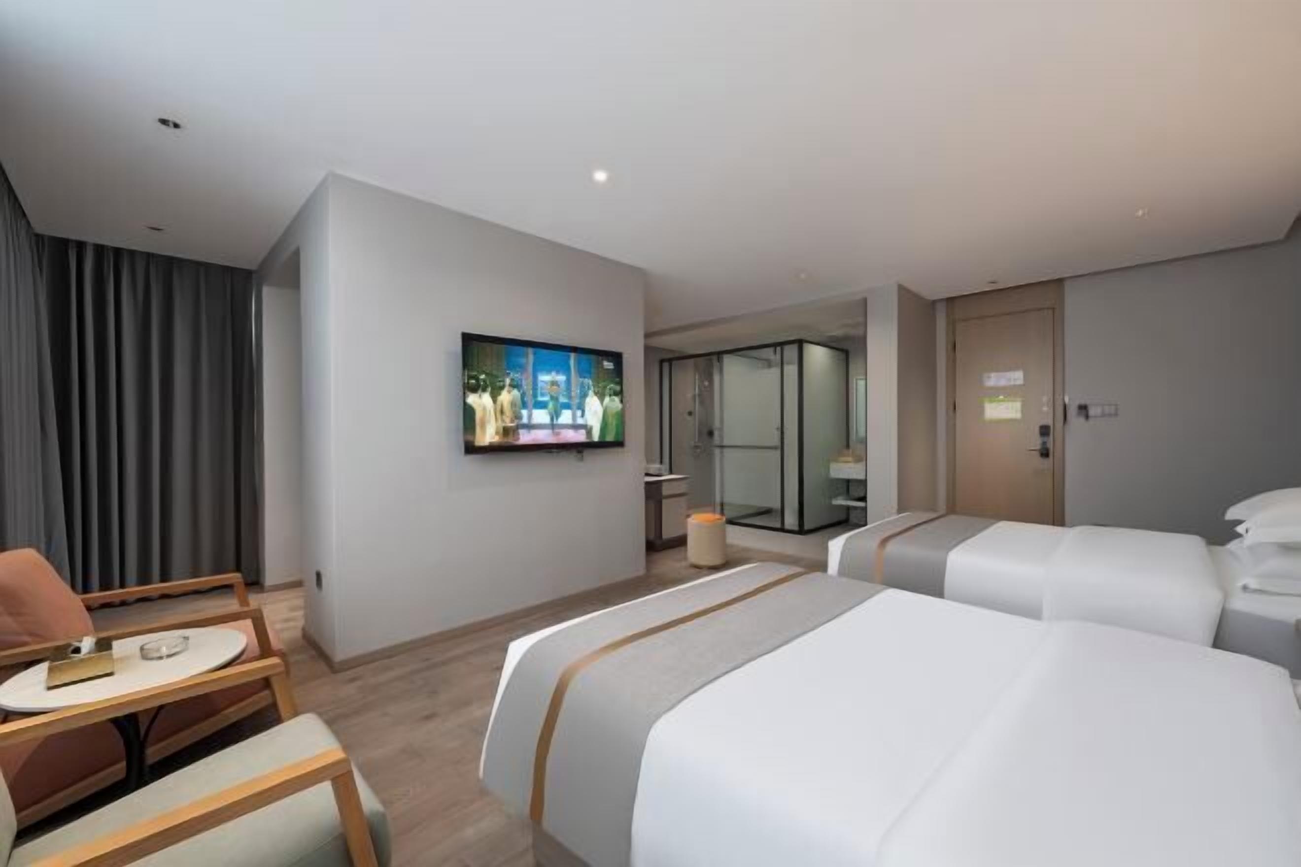 Een hotelkamer met twee bedden, een aan de muur bevestigde televisie, een tafeltje met een stoel, en een glazen deur naar een badkamer.