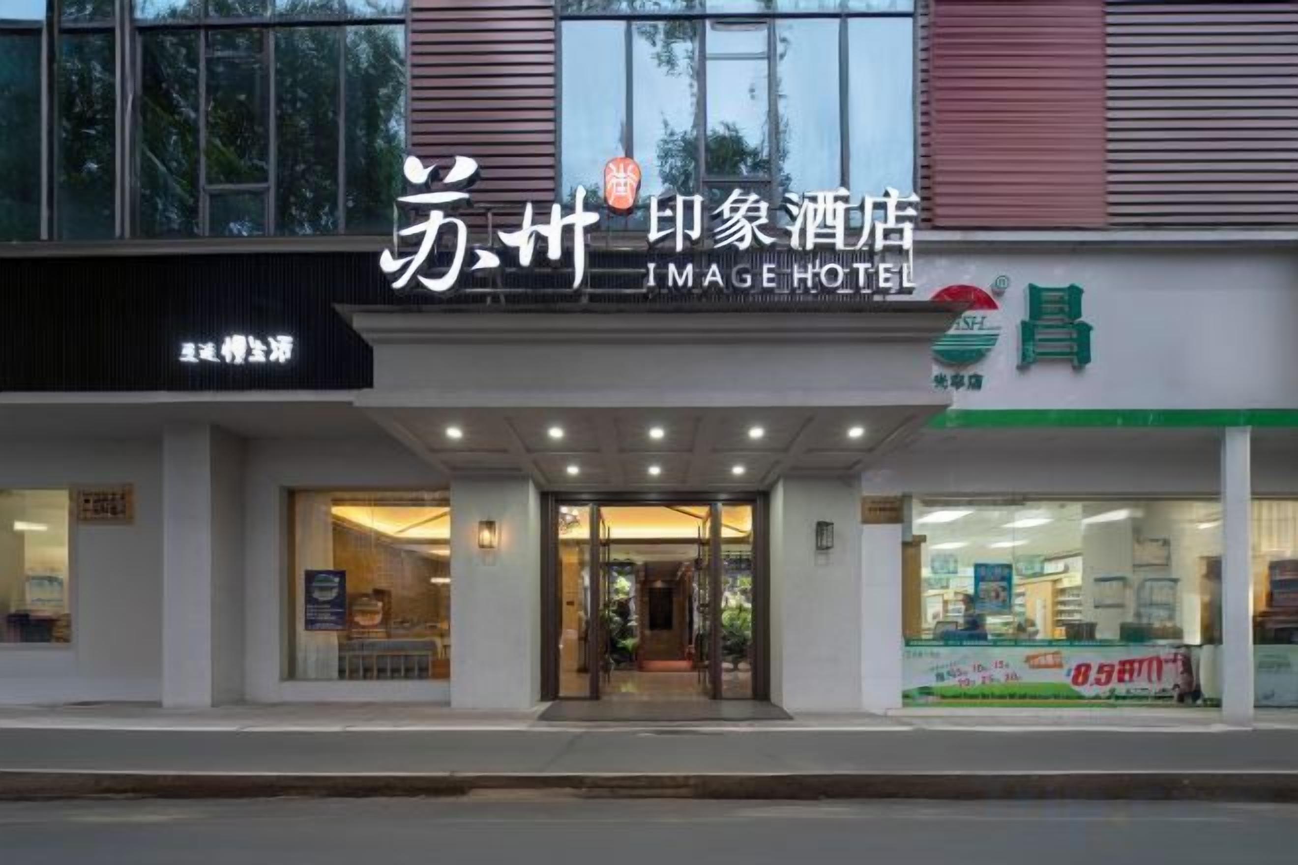 A hotel entrance with a sign that reads 'JIMAGE HOTEL' and a storefront with a green sign.