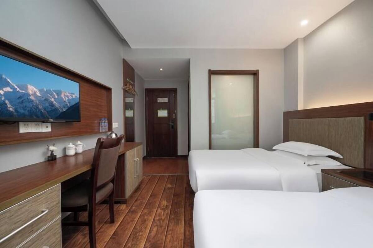 A hotel room with a TV, a desk, two beds, a chair, and a door.