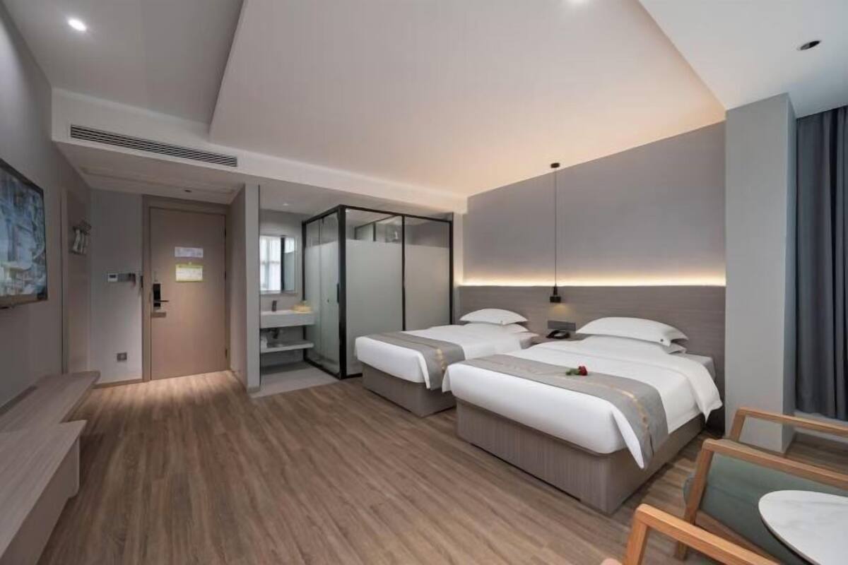 A modern hotel room with two beds, a sitting area, and a large mirror.