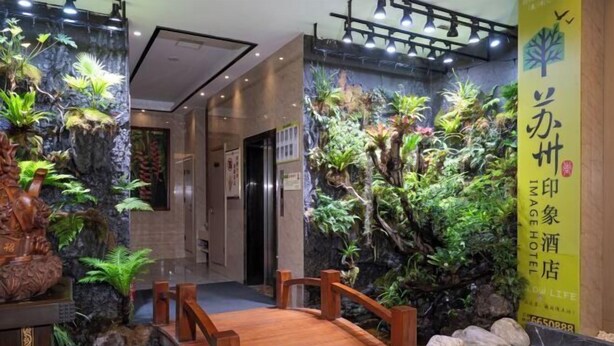 A hotel lobby with a wooden bridge, tropical plants, and a sign indicating the hotel name. - Suzhou Impression Hotel (Pingxiang)