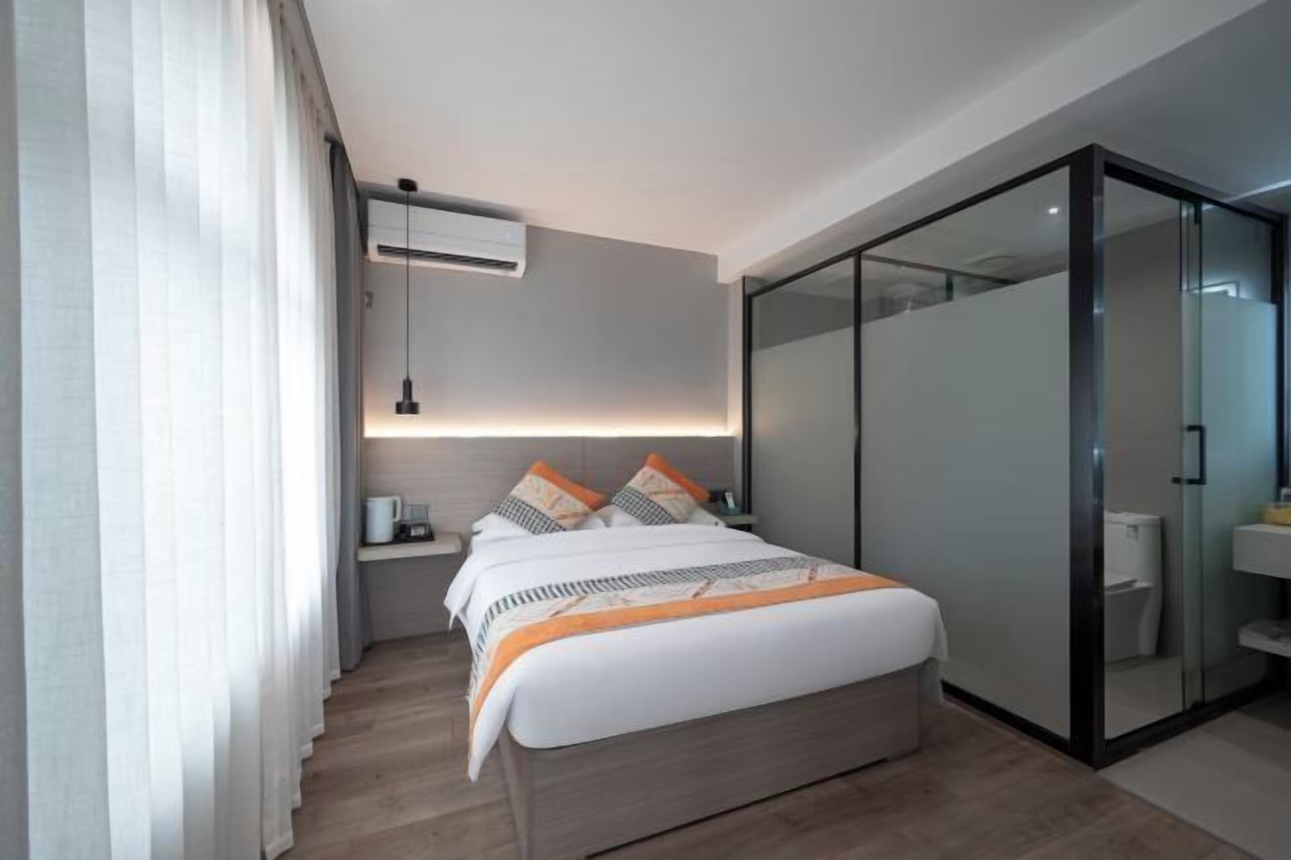 Een moderne hotelkamer met een bed, nachtkastje en een glazen inloopkast.