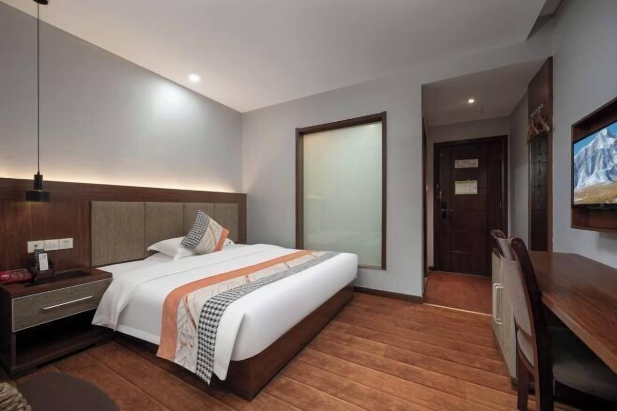 A hotel room with a bed, bedside table, lamp, and a TV on the wall.