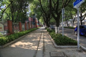 A tree-lined sidewalk with a metal fence on one side and a parked car on the other. - Bu can't thirst Wisdom Hotel (Shanghai)