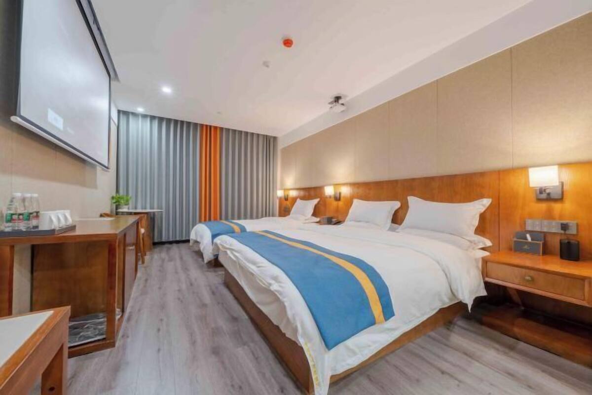 A hotel room with two beds, wooden headboards, a desk with a chair, and a TV screen.