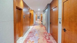 Un pasillo de hotel con puertas de madera, alfombra estampada y suelo de baldosas.