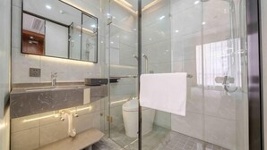 Un baño moderno con cabina de ducha de vidrio, tocador de mármol y un espejo grande.