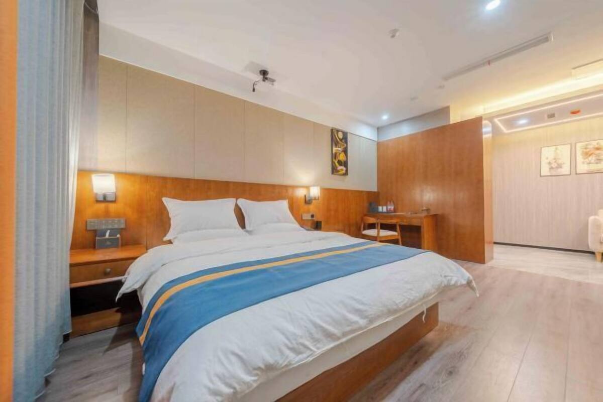 A modern hotel room with a large bed, bedside tables, a wooden headboard, and a wall-mounted artwork.