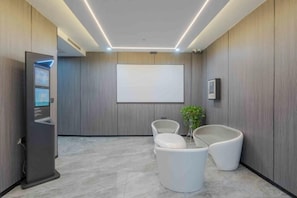 Una zona d'espera moderna amb una taquilla d'informació, seients, una pantalla gran i una planta.