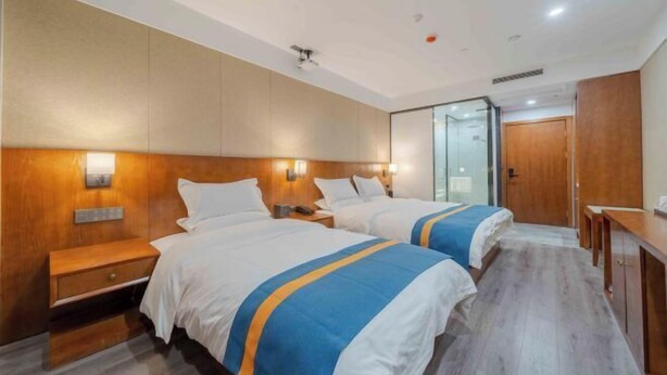 Habitación de hotel con dos camas, cabeceros de madera, mesitas de noche, un escritorio y un espejo.