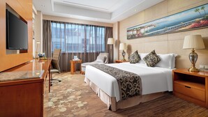 Een hotelkamer met een groot bed, een bureau, een televisie en een schilderij aan de muur.