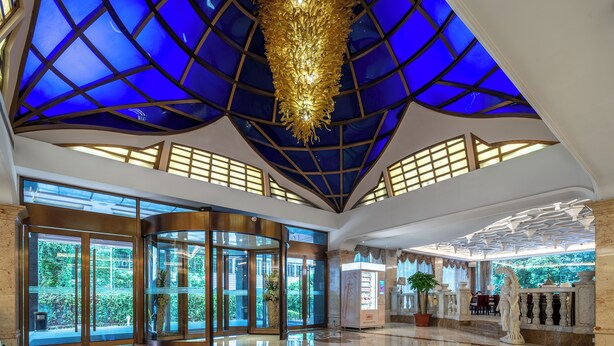 Een ruime lobby met een hoge plafond, grote glazen deuren en een centrale kroonluchter.