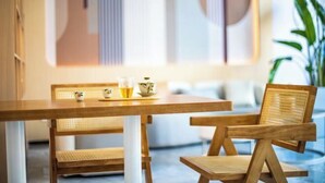 Una mesa de comedor de madera con una silla tejida y un banco, acompañados por una tetera y tazas.