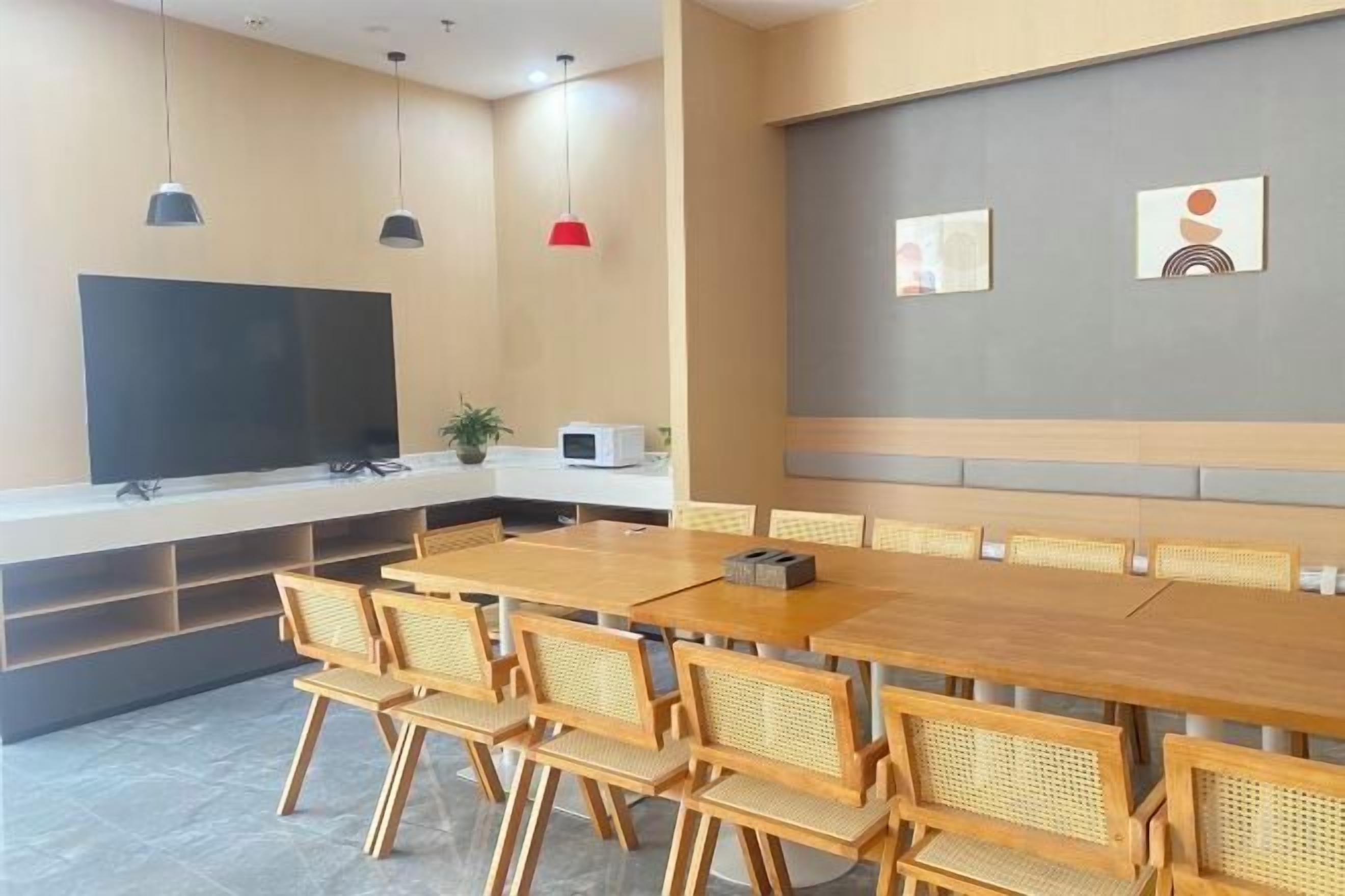 A modern meeting room with a long table, chairs, a flat-screen TV, and a small kitchen area.