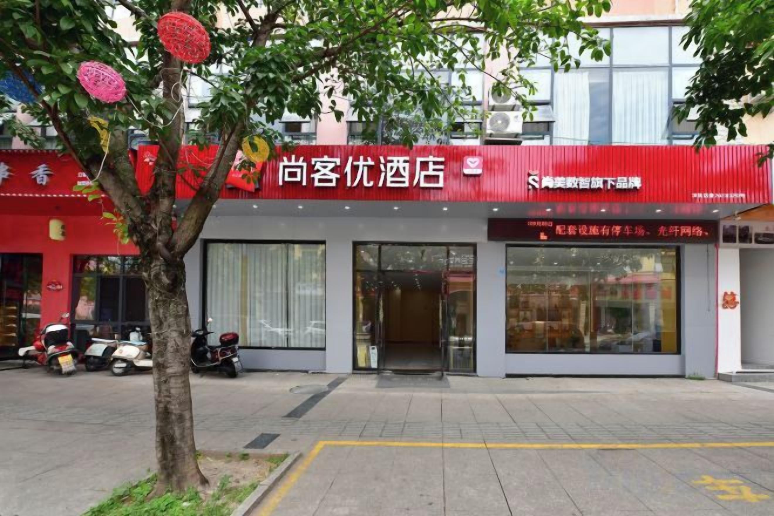 A hotel with a red facade, large windows, and a tree in front.