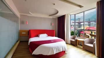A hotel room with a large bed, a small table, a chair, and a view of a bridge and mountains.