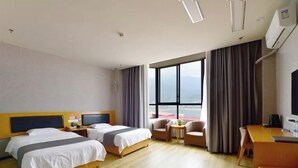 Habitación de hotel con dos camas, un escritorio, una silla, una mesita y un ventanal con vistas.