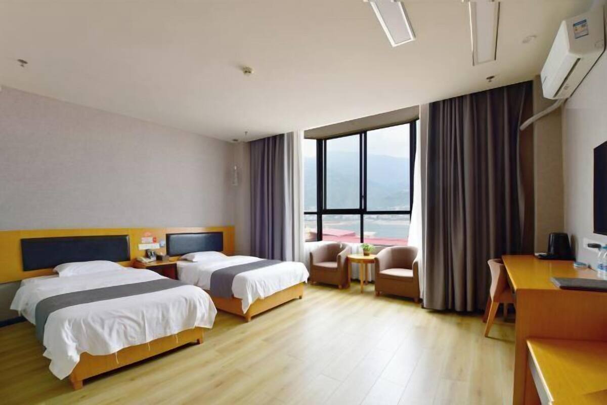 Habitació d'hotel amb dos llits, escriptori, cadira, taula petita i un finestral gran que ofereix una vista.