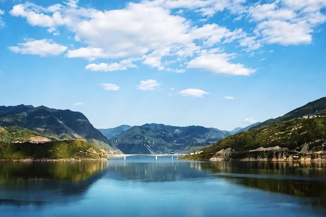 A calm lake with mountains, a bridge, and clear skies.