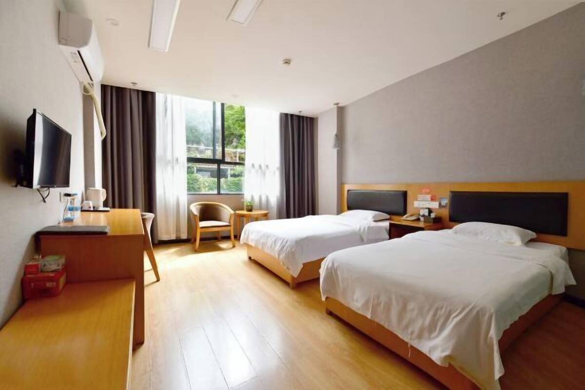 Habitació d'hotel amb dos llits, escriptori, cadira, televisió i finestra amb cortines.