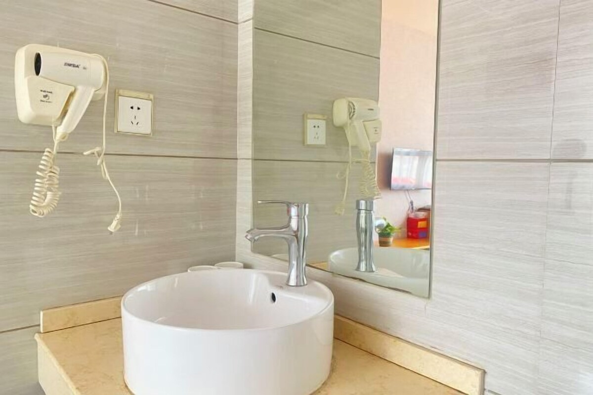 Ein Badezimmer mit einem weißen Waschbecken, einem Spiegel und einem an der Wand befestigten Föhn.