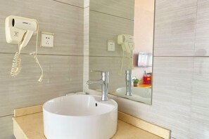 Ein Badezimmer mit einem weißen Waschbecken, einem Spiegel und einem an der Wand befestigten Föhn.