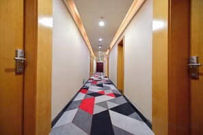 Un couloir d’hôtel avec des portes en bois, une moquette à motifs et un plafond doté d’un éclairage encastré.