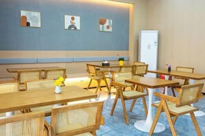 Un espace repas avec des tables et des chaises en bois, un réfrigérateur blanc et des œuvres d’art murales.
