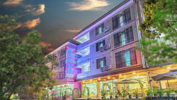 A multi-story hotel with a prominent neon sign, outdoor seating area, and a visible storefront.
