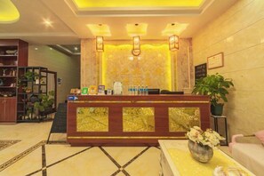 Un espace d’accueil d’hôtel comprenant un comptoir de réception en bois, un coin salon agrémenté d’un vase de fleurs et un mur où sont accrochés des certificats encadrés.