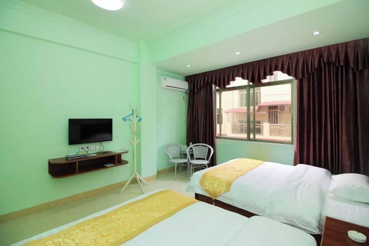 A hotel room with two beds, a TV, a desk, and a window with curtains.