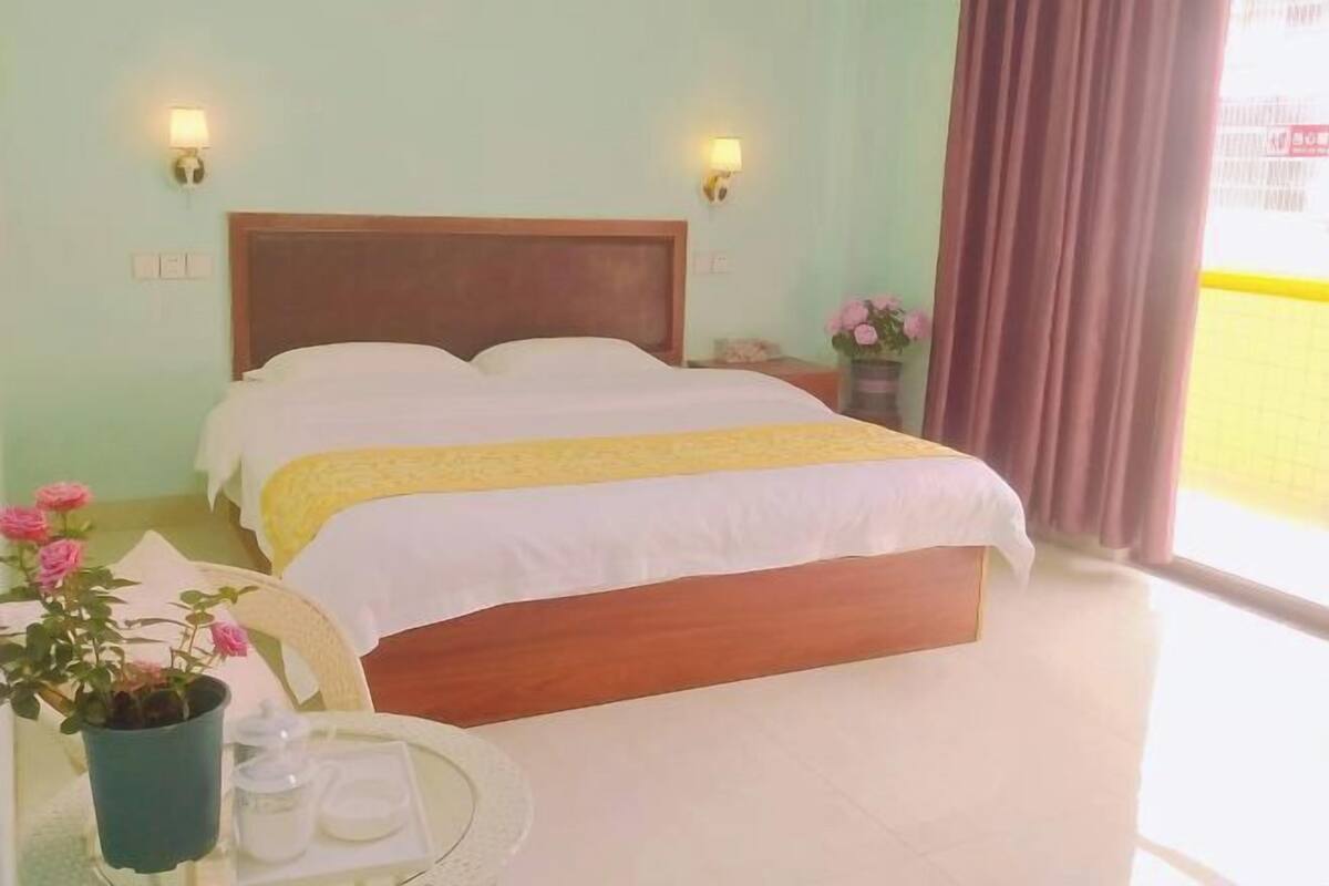 A hotel room with a bed, bedside lamps, a potted plant, and a window with curtains.