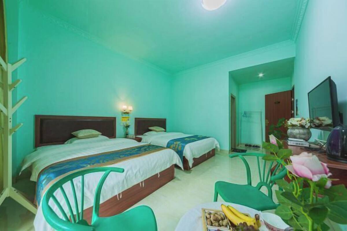 A room with two beds, a desk with a computer, a chair, and a table with fruits.