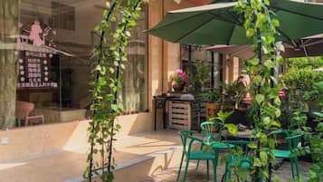 An outdoor seating area with green chairs and a table, surrounded by potted plants and a green umbrella.