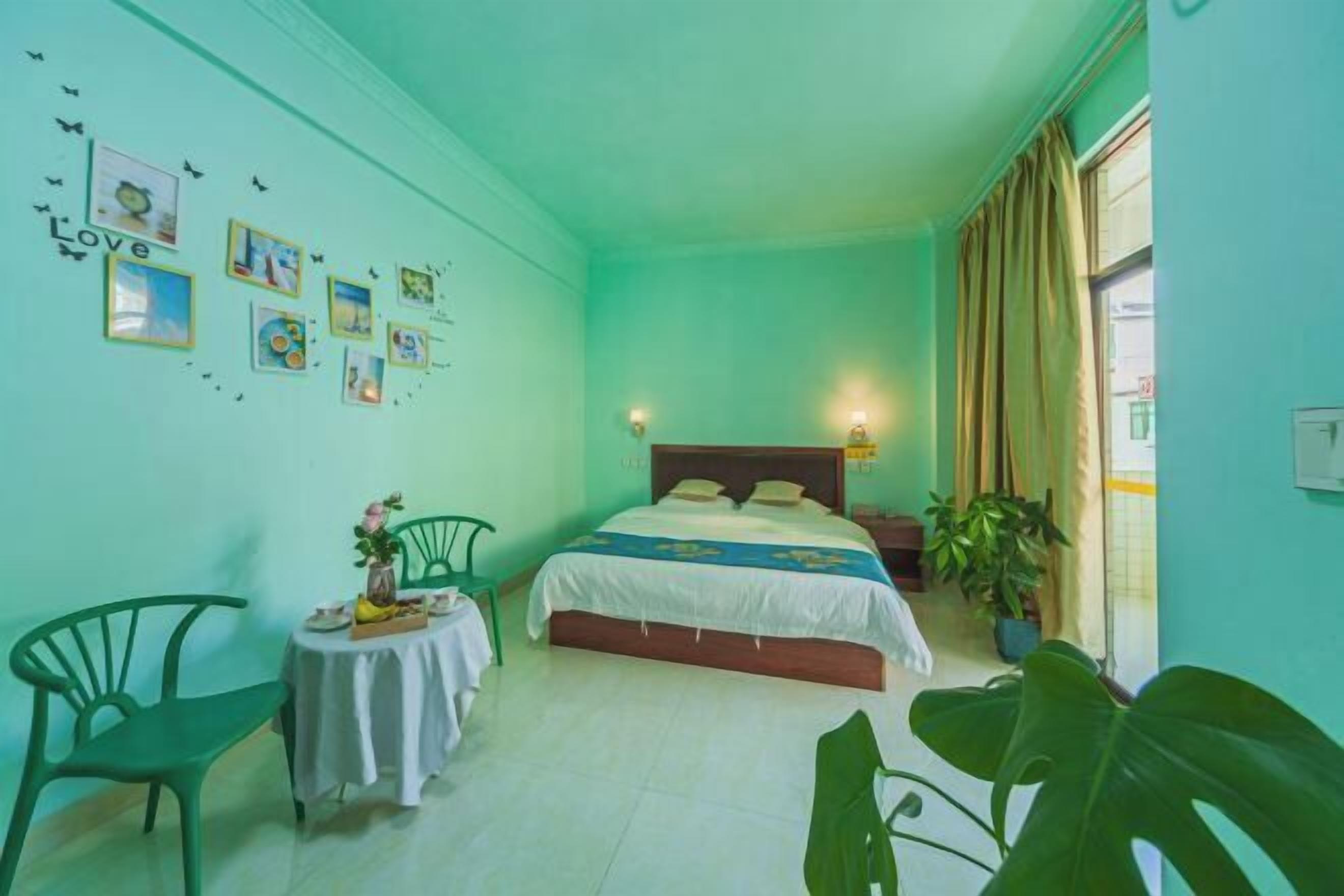 A room with a bed, a small table with a vase and a chair, and a window with curtains.