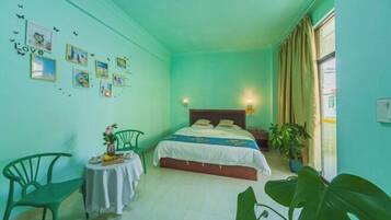 A room with a bed, a small table with a vase and a chair, and a window with curtains.