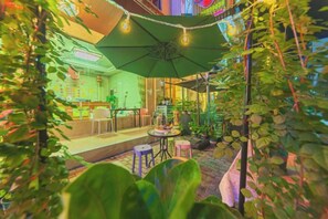 Un jardín interior con mesas y sillas, rodeado de plantas y un gran paraguas.