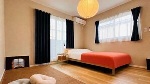 Una camera da letto con un letto, due finestre con tende, un condizionatore d'aria a parete, pavimento in legno e un piccolo comodino.