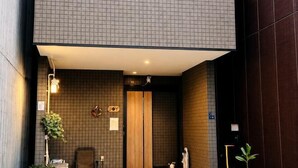 A modern bathroom with a tiled wall, a wooden door, and a towel rack. - Joy Home Tankachaya (Osaka)