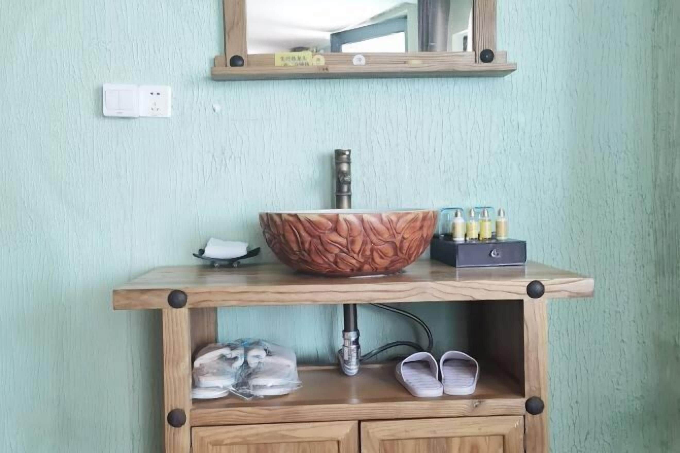 Ein Badezimmer mit Waschtisch aus Holz, einer großzügigen Schüssel als Waschbecken, einem Spiegel darüber und einem Ablagebereich für Toilettenartikel.