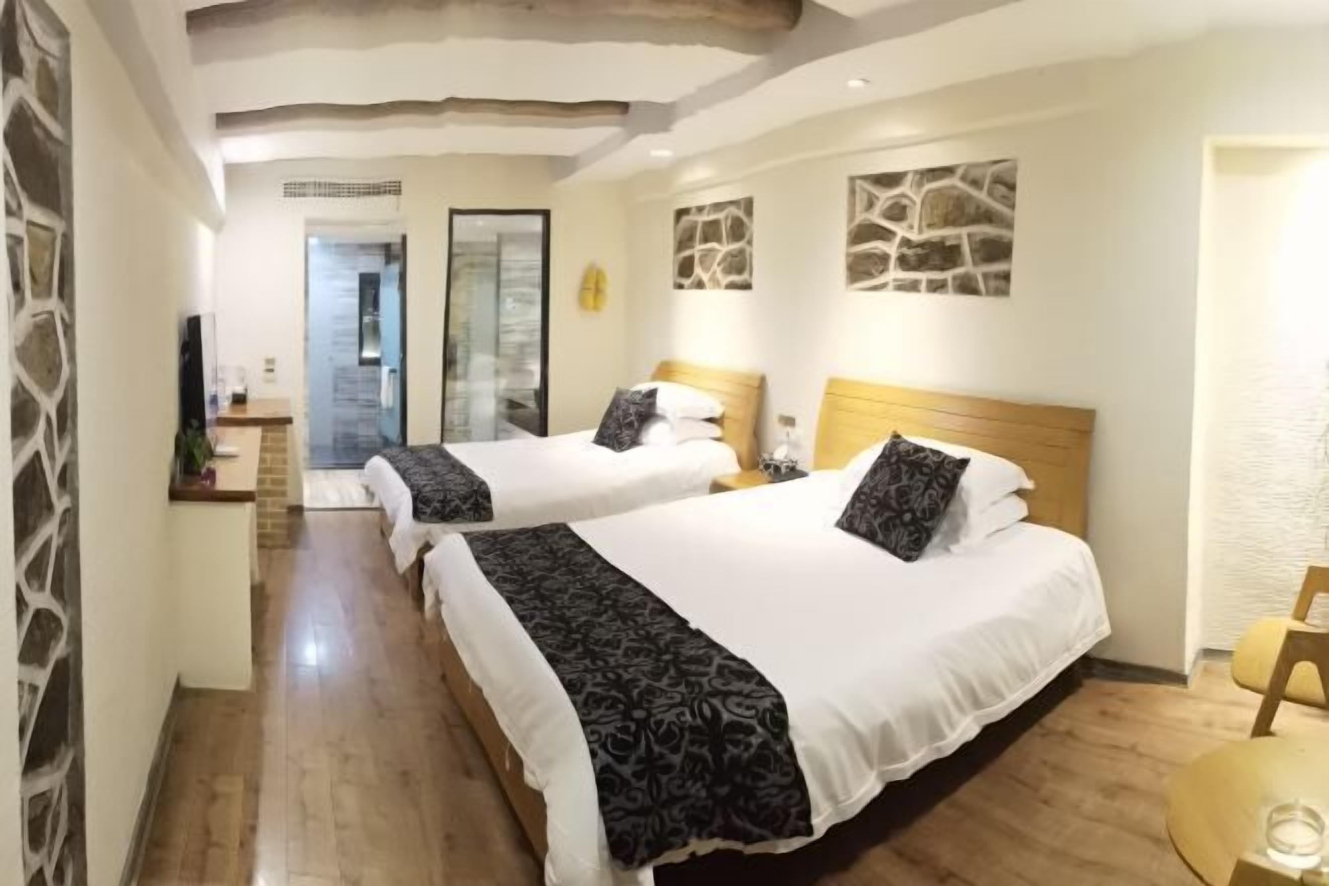 Habitación de hotel con dos camas, piso de madera, una mesita y una obra de arte colgada en la pared.